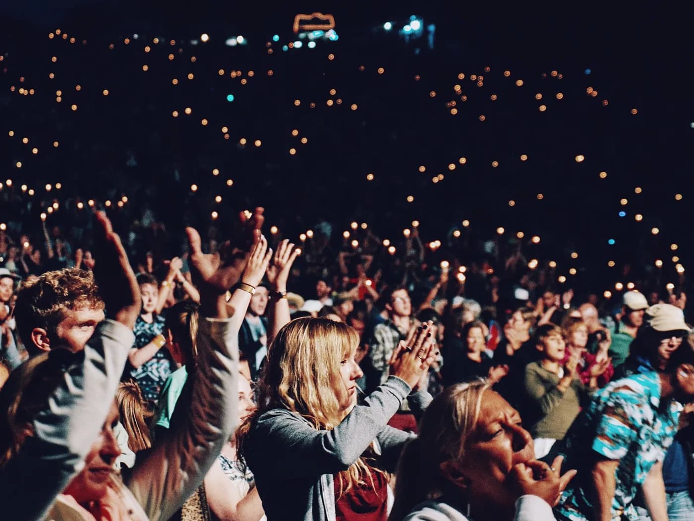 A capacity crowd with hands raised at an evening gala